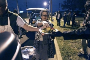 Joan Cheever, founder of The Chow Train, puts a piece of bread on a plate given to an individual at Maverick Park 