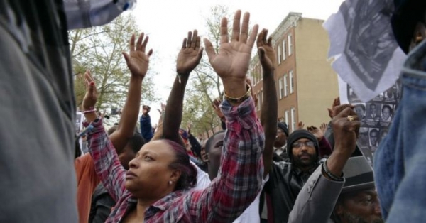 Residents kneel down, raising their hands to the sky behind concrete barriers placed there to expand the barriers of the Western District of the Baltimore Police as marchers take to the streets for another day of protests over the death of local resident Freddie Gray, while in police custody. 
