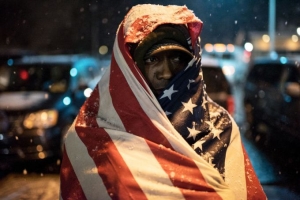  A protester covered in a U.S. flag stands in front of Ferguson Police Department as the snow falls, in Ferguson, Mo. on Nov. 26, 2014. 